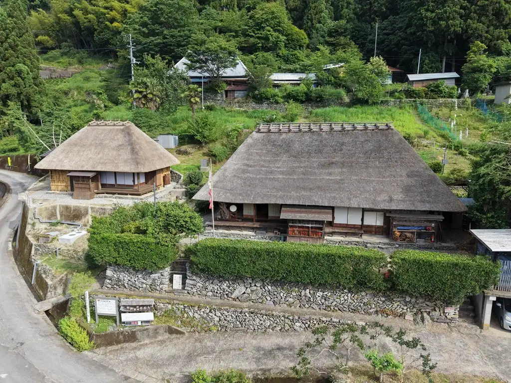 山の斜面に並ぶ二つの茅葺き建築。左が隠居屋、右が主屋
