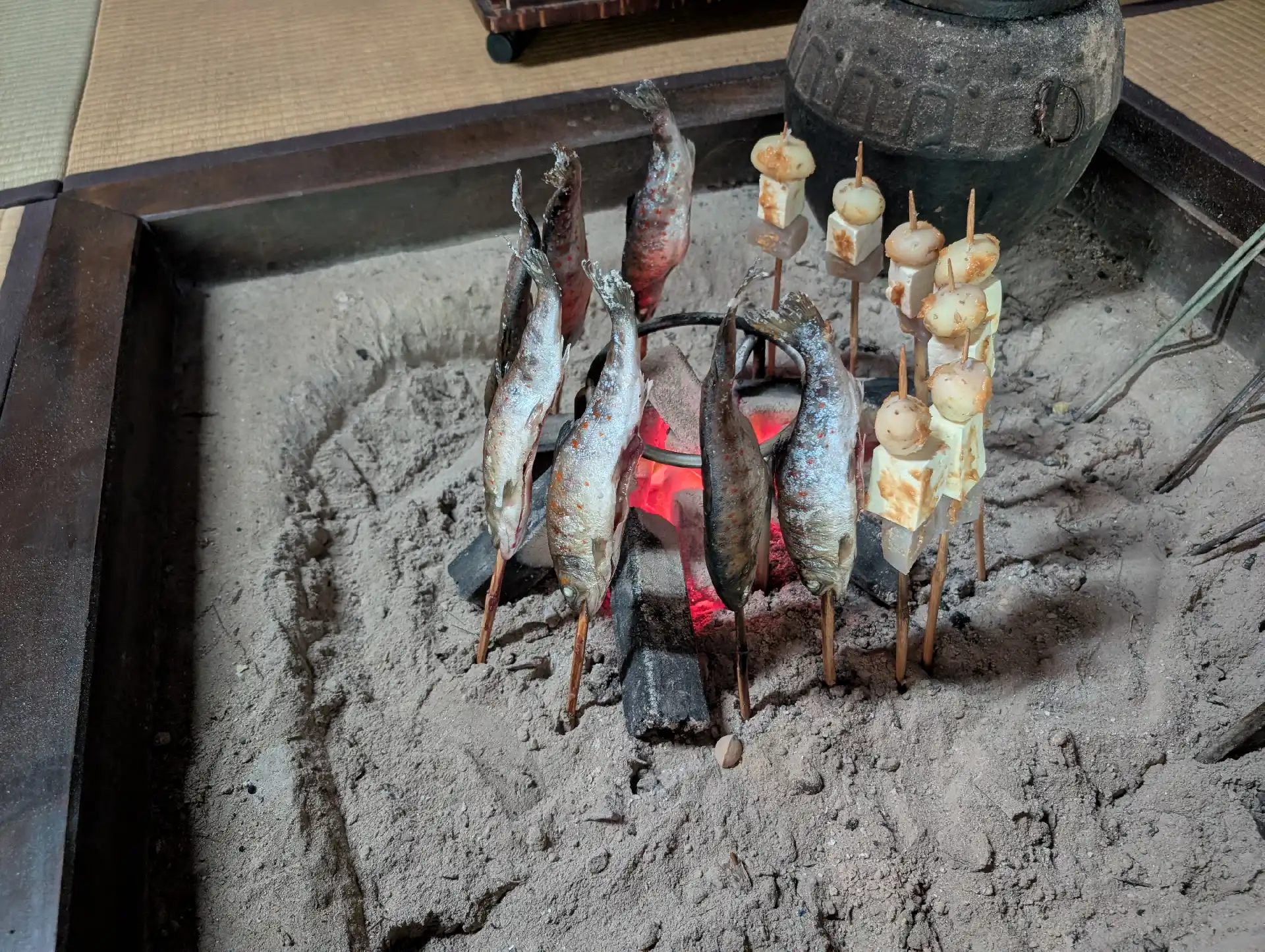 赤い炭火のそばで焼く、串に刺した川魚と田楽