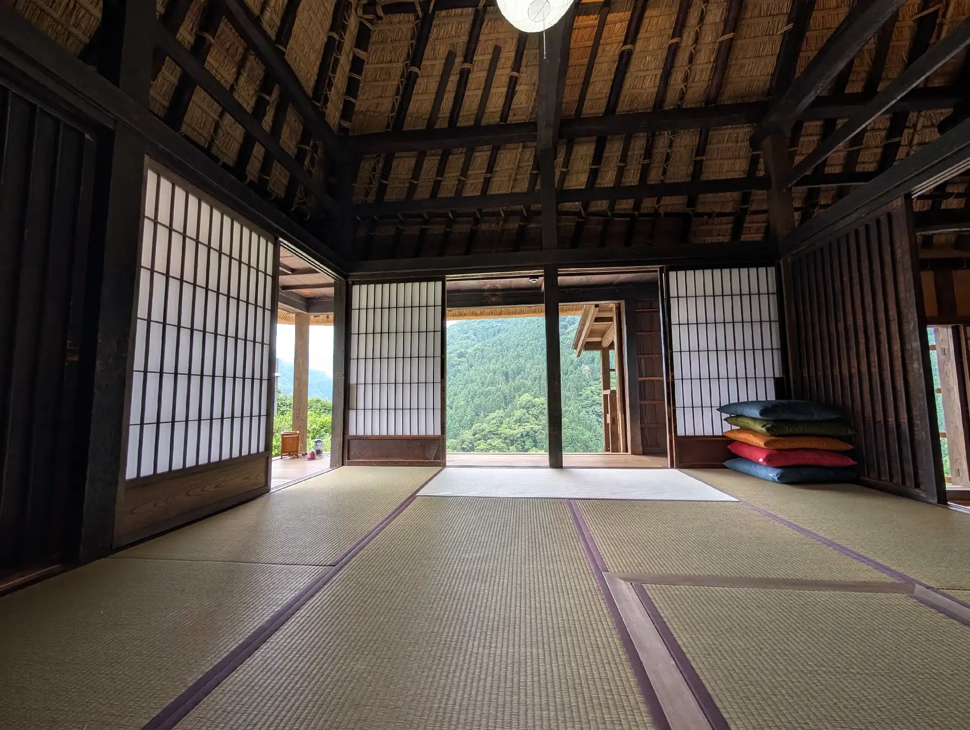 太い梁が渡る畳の和室。開いた障子の向こうに山の緑が見える